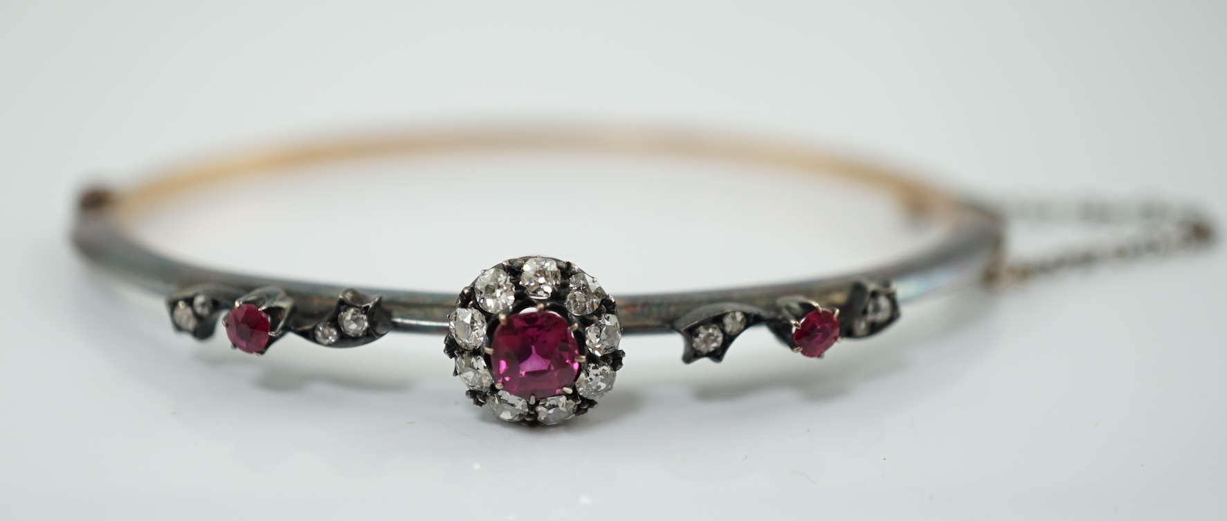 A late Victorian gold and silver, ruby and diamond cluster set hinged bangle